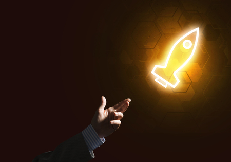 Rocket glowing icon and businessman hand on dark backgroundの写真素材