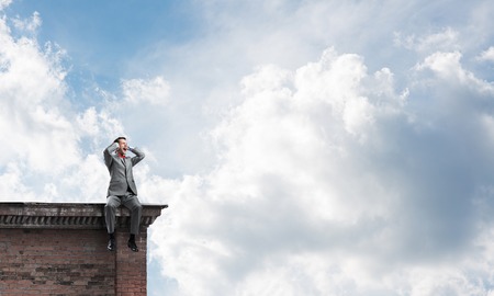 Frustrated businessman sitting on building top and closing ears with handsの写真素材