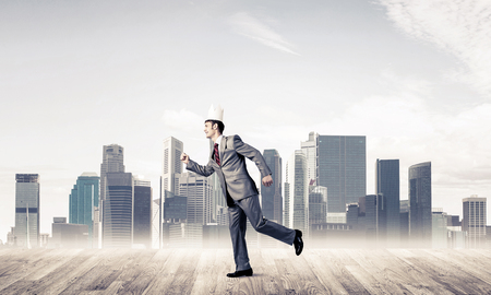 Young handsome businessman wearing white paper crown running in a hurryの写真素材