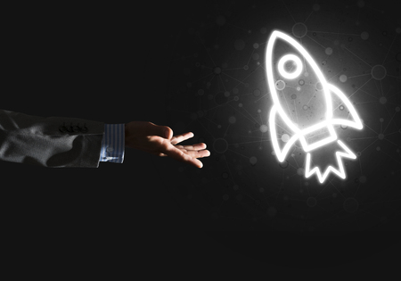 Rocket glowing icon and businessman hand on dark backgroundの写真素材