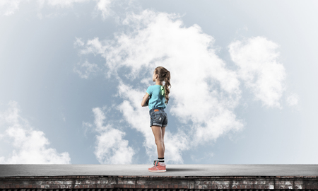 Cute kid girl standing on building roof with hands crossed on chestの写真素材