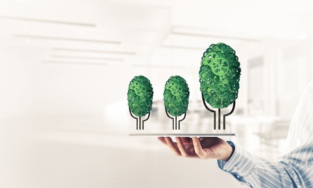Close of businessman holding tablet pc with green tree made of gears and cogwheels. Mixed mediaの写真素材