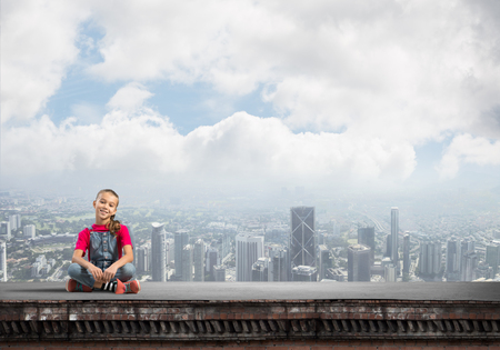 Cute kid girl sitting on building roof and looking in cameraの写真素材