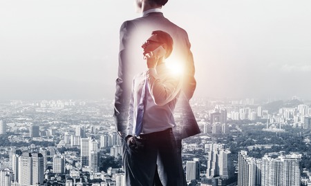 Double exposure of elegant businessman standing with back and talking his mobile phoneの写真素材