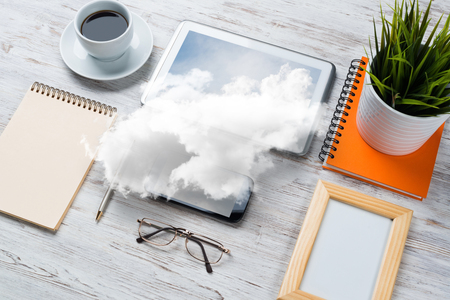 Top view of modern workplace with office stuff and cloud above presenting still office life. Mixed media.の写真素材