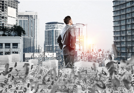 Young confident businessman in suit standing among flying letters with cityscape and sunlight on background. Mixed media.の写真素材