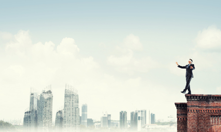 Businessman with blindfolder on eyes walking on building topの写真素材