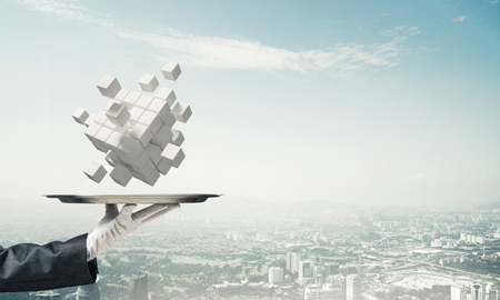 Cropped image of waiters hand in white glove presenting multiple cubes on metal tray with cityscape view on background. 3D rendering.の写真素材