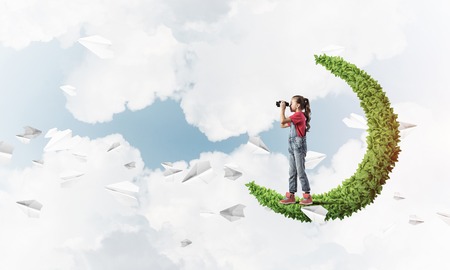 Cute kid girl on green moon and looking in binocularsの写真素材