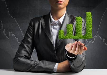 Businessman in suit presenting green plant in form of growing graph in hands with business sketches on background.の写真素材
