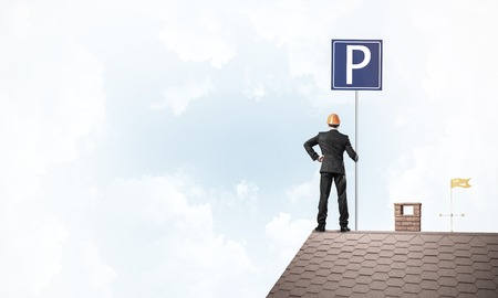 Businessman on house top holding car parking board and viewing city. Mixed mediaの写真素材