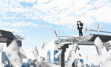 Businessman in suit looking in binoculars while standing among flying papers on broken bridge with cityscape on background. 3D rendering.の写真素材
