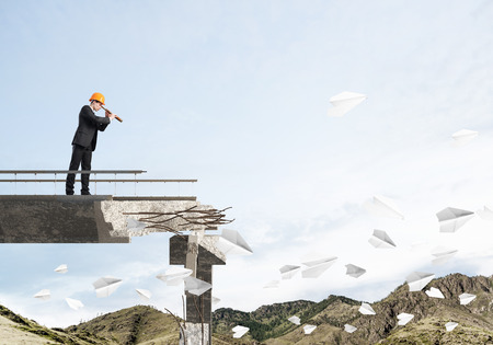 Engineer in suit and helmet looking in spyglass while standing among flying paper planes on broken bridge with skyscape and nature view on background. 3D rendering.の写真素材