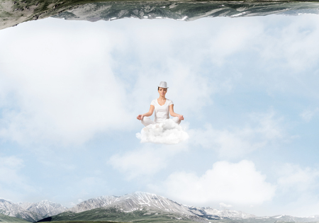 Young woman keeping eyes closed and looking concentrated while meditating on cloud in the air between two nature worlds.の写真素材