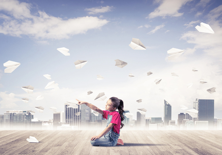 Cute kid girl sitting on wooden floor and paper planes flying aroundの写真素材