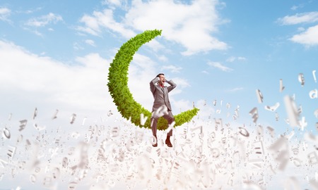 Frustrated businessman sitting on green moon and closing ears with handsの写真素材