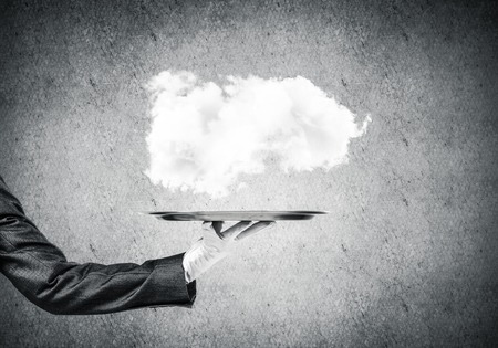 Closeup of waitress's hand in glove presenting white cloud on metal tray with gray concrete wall on...