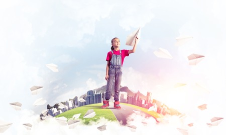 Cute kid girl on city floating island throwing paper planeの写真素材