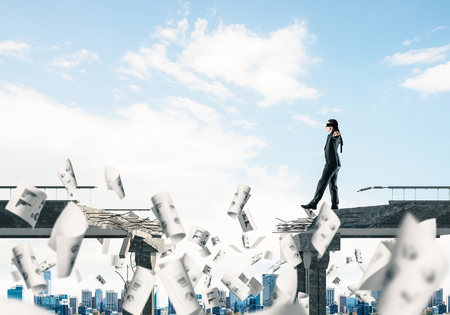 Businessman walking blindfolded among flying papers on concrete bridge with huge gap as symbol of hidden threats and risks. Cityscape view on background. 3D rendering.の写真素材