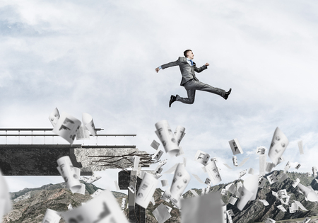 Businessman jumping over gap in bridge among flying papers as symbol of overcoming challenges. Skyscape and nature view on background. 3D rendering.の写真素材