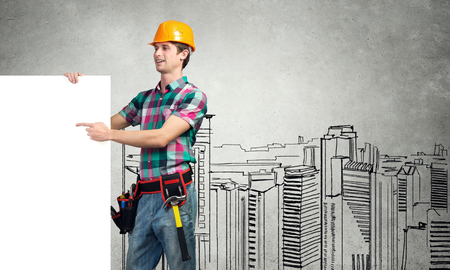 Young builder man pointing with finger at white blank banner. Place your textの写真素材