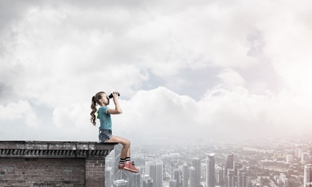 Cute girl of school age on building roof looking in binocularsの写真素材