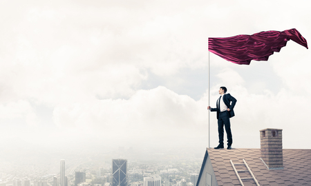 Businessman standing on house roof and red holding flag. Mixed mediaの写真素材