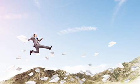 Businessman in suit running in the air among flying paper planes as symbol of active life position. Skyscape with sunlight and nature view on background. 3D rendering.の写真素材