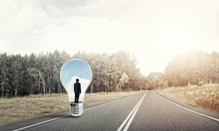 Young businessman trapped inside of light bulb on asphalt roadの写真素材