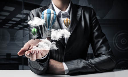 Closeup of business woman in suit presenting flying aerostate among clouds in her palm with dark office view on background. 3D rendering.の写真素材