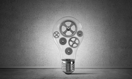 Glass lightbulb with multiple gears inside placed in empty room with grey wall on background. 3D rendering.の写真素材