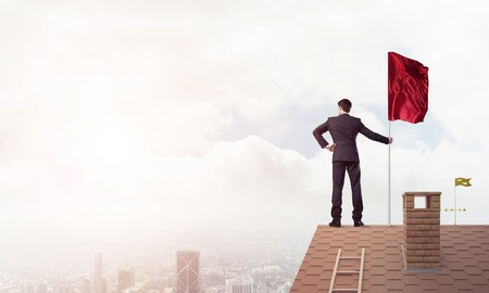 Businessman standing on house roof and red holding flag. Mixed mediaの写真素材