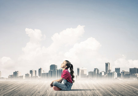 Cute kid girl sitting on wooden floor and looking upの写真素材