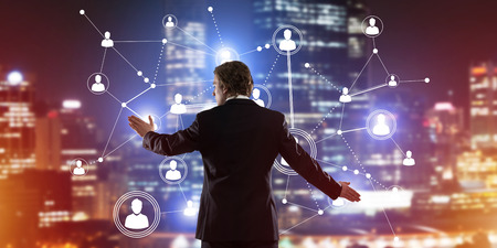 Back view of businessman against night cityscape working with social connection media conceptの写真素材