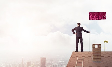 Businessman standing on house roof and red holding flag. Mixed mediaの写真素材