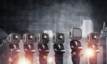 Business women in suits with old TV instead of their heads keeping arms crossed while standing among flying lightbulbs and against analytical charts drawn on wall on background.の写真素材