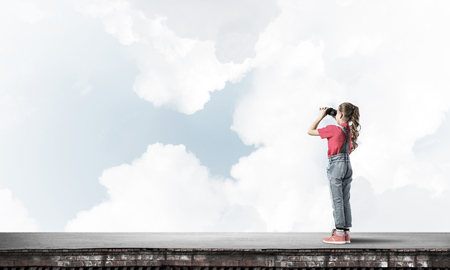 Cute girl of school age on building roof looking in binocularsの写真素材