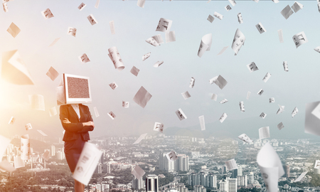 Cropped image of business woman in suit with monitor instead of head keeping arms crossed while standing outdoors among flying papers with cityscape view on background.の写真素材