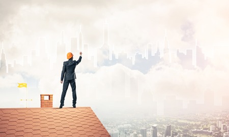 Engineer man standing with back on house roof and drawing city. Mixed mediaの写真素材