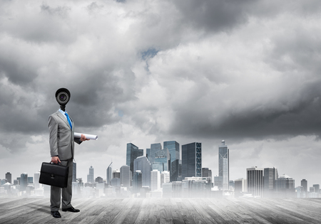 Faceless businessman with camera zoom instead of head against cityscape backgroundの写真素材