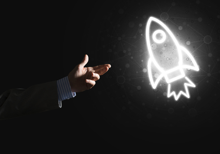 Rocket glowing icon and businessman hand on dark backgroundの写真素材