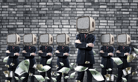 Businessmen in suits with old TV instead of their heads keeping arms crossed while standing in a row among flying euro banknotes in empty room with gray wall on background.の写真素材