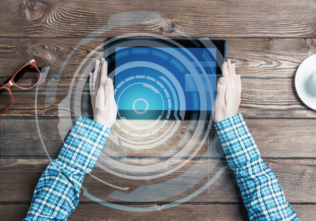 Top view of woman in checked shirt sitting at wooden table with tablet pcの写真素材