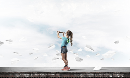 Cute kid girl standing on house roof and looking in spyglassの写真素材