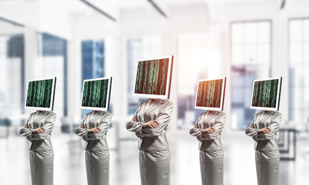 Business women in suits with monitors instead of their heads keeping arms crossed while standing in a row inside office building.の写真素材