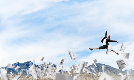 Attractive business woman in suit jumping in the air among flying papers as symbol of active life position. Skyscape and nature view on background. 3D rendering.の写真素材