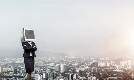Cropped image of business woman in suit with monitor instead of head keeping arms crossed while standing outdoors with cityscape view on background.の写真素材