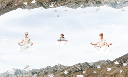 Young family keeping eyes closed and looking concentrated while meditating on clouds among flying paper planes and between two nature worlds.の写真素材