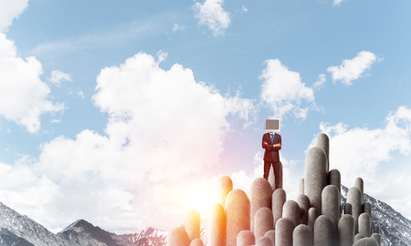 Businessman in suit with monitor instead of head keeping arms crossed while standing on the top of stone columns with beautiful landscape on background.の写真素材