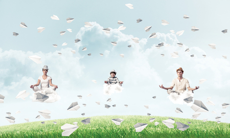 Young family keeping eyes closed and looking concentrated while meditating on clouds among flying paper planes with bright and beautiful landscape on background.の写真素材